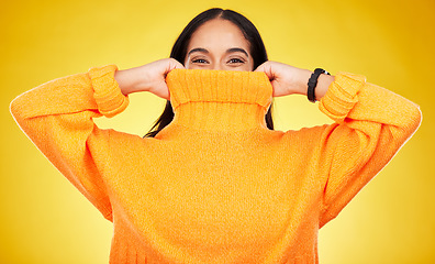 Image showing Happy, cover and portrait of a woman with a jersey isolated on a yellow background in a studio. Hiding, winter and a girl holding a jumper up for covering, warmth and bad weather on a backdrop