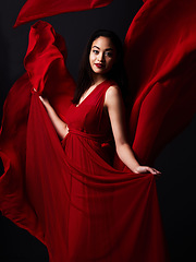 Image showing Portrait of woman, art and fashion, fabric on dark background with beauty and aesthetic movement. Flowing silk motion, fantasy and artistic model with smile in red creative designer dress in studio.