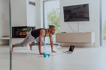 Image showing Training At Home. Sporty man doing training while watching online tutorial on laptop, exercising in living room, free space