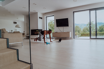 Image showing Training At Home. Sporty man doing training while watching online tutorial on laptop, exercising in living room, free space