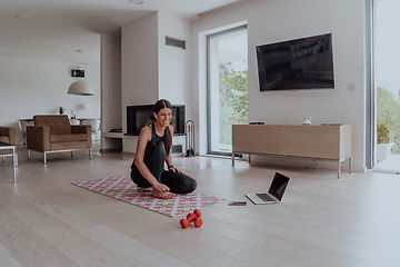 Image showing Young Beautiful Female Exercising, Stretching and Practising Yoga with Trainer via Video Call Conference in Bright Sunny Loft Apartment. Healthy Lifestyle, Wellbeing and Mindfulness Concept.