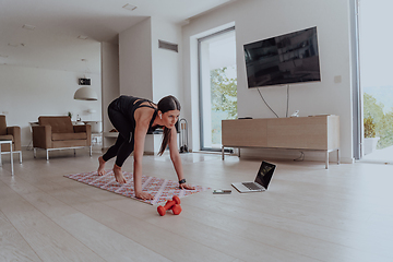 Image showing Young Beautiful Female Exercising, Stretching and Practising Yoga with Trainer via Video Call Conference in Bright Sunny House. Healthy Lifestyle, Wellbeing and Mindfulness Concept.