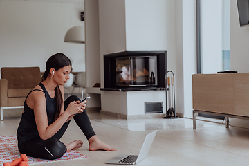 Image showing Young woman in sportswear using laptop and smartphone for online training in living room at home during corona virus and social distancing