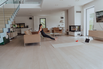 Image showing Young Beautiful Female Exercising, Stretching and Practising Yoga with Trainer via Video Call Conference in Bright Sunny Loft Apartment. Healthy Lifestyle, Wellbeing and Mindfulness Concept.