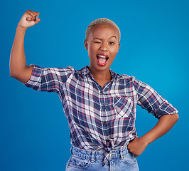 Image showing Wink, arm flex and portrait of black woman in studio for empowerment, confident and success. Achievement, hard work and pride with female isolated on blue background for power, strong or motivation