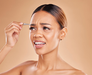 Image showing Beauty, pain and eyebrows with woman and tweezers in studio for clean, self care and cosmetics. Facial, plucking and shape with female model on brown background for hair removal, skincare or grooming