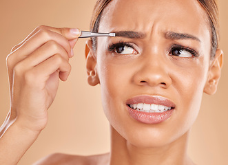 Image showing Pain, hair removal and eyebrows with woman and tweezers in studio for clean, self care and cosmetics. Facial, plucking and shape with female model on brown background for grooming and skincare