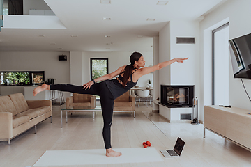 Image showing Young Beautiful Female Exercising, Stretching and Practising Yoga with Trainer via Video Call Conference in Bright Sunny House. Healthy Lifestyle, Wellbeing and Mindfulness Concept.