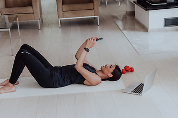 Image showing Sportswoman using a smartphone while resting and lying on floor of modern house