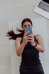 Image showing Sportswoman using a smartphone while resting and lying on floor of modern house