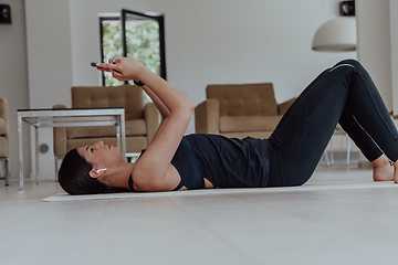 Image showing Sportswoman using a smartphone while resting and lying on floor of modern house