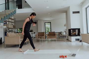 Image showing Young Beautiful Female Exercising, Stretching and Practising Yoga with Trainer via Video Call Conference in Bright Sunny Loft Apartment. Healthy Lifestyle, Wellbeing and Mindfulness Concept.