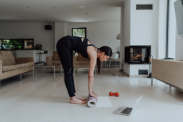 Image showing A young woman in sports clothes preparing sports equipment for online training in her living room