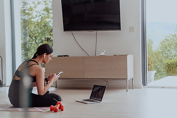 Image showing Young woman in sportswear using laptop and smartphone for online training in living room at home during corona virus and social distancing