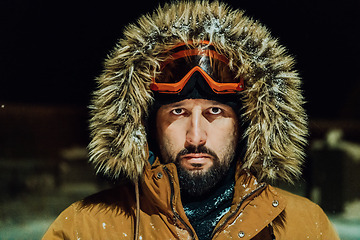 Image showing Head shot of a man in a cold snowy area wearing a thick brown winter jacket, snow goggles and gloves on a cold Scandinavian night. Life in the cold regions of the country.