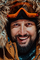 Image showing Head shot of a man in a cold snowy area wearing a thick brown winter jacket, snow goggles and gloves on a cold Scandinavian night. Life in the cold regions of the country.