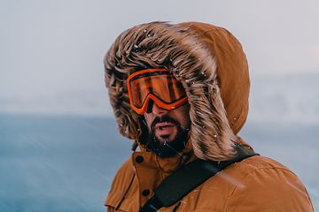 Image showing Headshot photo of a man in a cold snowy area wearing a thick brown winter jacket, snow goggles and gloves. Life in cold regions of the country.