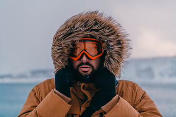 Image showing Headshot photo of a man in a cold snowy area wearing a thick brown winter jacket, snow goggles and gloves. Life in cold regions of the country.