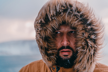 Image showing Headshot photo of a man in a cold snowy area wearing a thick brown winter jacket and gloves. Life in cold regions of the country.