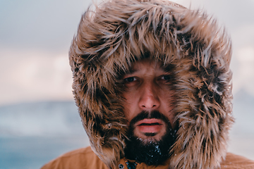 Image showing Headshot photo of a man in a cold snowy area wearing a thick brown winter jacket and gloves. Life in cold regions of the country.