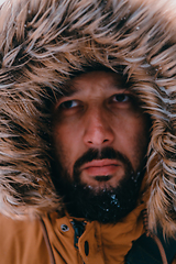 Image showing Headshot photo of a man in a cold snowy area wearing a thick brown winter jacket and gloves. Life in cold regions of the country.