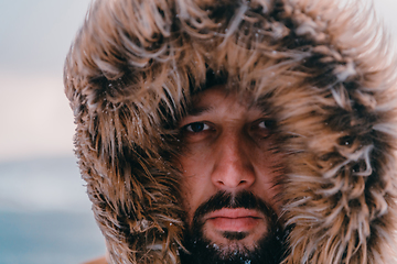 Image showing Headshot photo of a man in a cold snowy area wearing a thick brown winter jacket and gloves. Life in cold regions of the country.