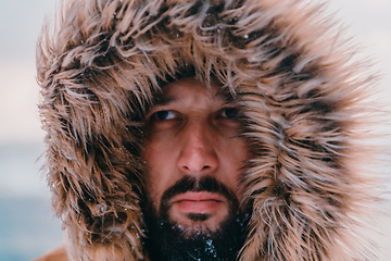 Image showing Headshot photo of a man in a cold snowy area wearing a thick brown winter jacket and gloves. Life in cold regions of the country.