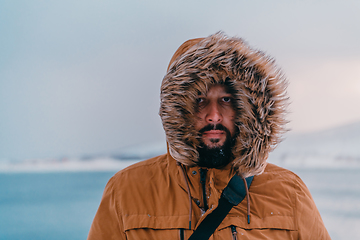 Image showing Headshot photo of a man in a cold snowy area wearing a thick brown winter jacket and gloves. Life in cold regions of the country.