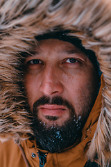 Image showing Headshot photo of a man in a cold snowy area wearing a thick brown winter jacket and gloves. Life in cold regions of the country.