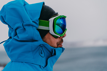 Image showing Headshot photo of a man in a cold snowy area wearing a thick blue winter jacket, snow goggles and gloves. Life in cold regions of the country.