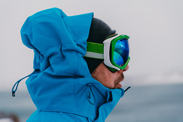 Image showing Headshot photo of a man in a cold snowy area wearing a thick blue winter jacket, snow goggles and gloves. Life in cold regions of the country.