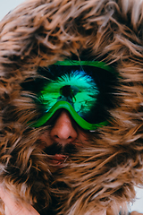 Image showing Headshot photo of a man in a cold snowy area wearing a thick brown winter jacket, snow goggles and gloves. Life in cold regions of the country.