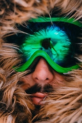 Image showing Headshot photo of a man in a cold snowy area wearing a thick brown winter jacket, snow goggles and gloves. Life in cold regions of the country.