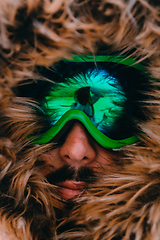 Image showing Headshot photo of a man in a cold snowy area wearing a thick brown winter jacket, snow goggles and gloves. Life in cold regions of the country.