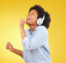 Image showing Black woman, singing with headphones and freedom, music and happiness with invisible mic on yellow studio background. Happy female, carefree and radio, audio streaming, fun and energy with technology