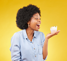 Image showing Black woman, cupcake and excited or happy in studio while eating sweet food on a yellow background. African female model with snack, dessert or cake for happiness, birthday or celebration mockup