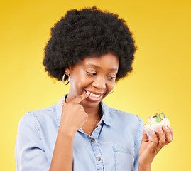 Image showing Woman, cupcake and studio with thinking, diet and temptation for guilt with junk food by yellow background. African model, cake and choice for unhealthy, nutrition and sweets with discipline for meal