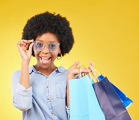 Image showing Fashion, portrait and black woman with shopping bags, smile and excited for sale in studio on yellow background. Face, shopper and girl customer cheerful after boutique, retail or store discount