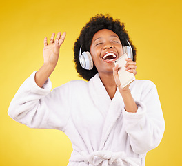 Image showing Black woman, music headphones and singing with phone in studio isolated on a yellow background. Karaoke singer, bathrobe and happy female dance with mobile microphone while streaming podcast or radio