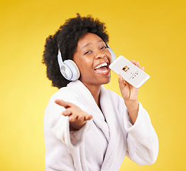 Image showing Black woman, music headphones and singing with phone in studio isolated on a yellow background. Karaoke singer, bathrobe and face portrait of happy female with mobile while streaming podcast or radio