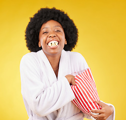 Image showing Funny face, portrait and black woman eating popcorn in studio isolated on a yellow background. Comic smile, food and laughing, hungry and happy female eat corn or snack in morning gown or bathrobe.