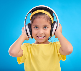 Image showing Music, headphones and listening with portrait of girl in studio for streaming, mobile radio and audio. Technology, media and youth with child isolated on blue background for natural, happy and songs