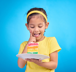 Image showing Food, happy and child with rainbow cake on blue background for birthday, celebration and party mockup. Comic, smile and excited young girl with sweet snack in studio with pastry, dessert and eating