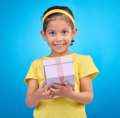 Image showing Gift, box and smile with portrait of girl in studio for celebration, shopping and birthday event. Happiness, surprise and present with child for party, giveaway or product isolated on blue background