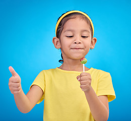 Image showing Candy, happy and child with lollipop and thumbs up on blue background with happiness, smile and excited. Party, childhood and young girl with hand sign eating sweets snack, sugar and treats in studio