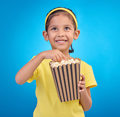 Image showing Popcorn, eating and watching movie with girl in studio for food, cinema and comedy. Laugh, television and film with child and snack for streaming, subscription and tv isolated on blue background