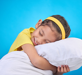 Image showing Young girl smile, pillow and sleep in a studio feeling tired, fatigue and ready for dreaming. Isolated, blue background and happy little child with pillows and closed eyes for sleeping, rest and nap