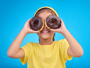Image showing Donut, eyes and covering face of playful cute girl with food isolated against a studio blue background with a smile. Adorable, happy and young child or kid excited for sweet sugar doughnuts