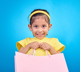 Image showing Girl smile, portrait and gift bags from birthday party, event or celebration with a present in studio. Shop choice, bag and little child looking at presents with isolated and blue background with kid