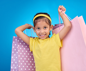 Image showing Girl, shopping portrait and gift bags from birthday party, event or celebration with a present in studio. Shop sale, bag and little child with presents with isolated and blue background with a kid